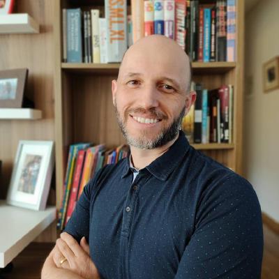 Photograph of white male wearing a blue polo shirt in front of a bookcase